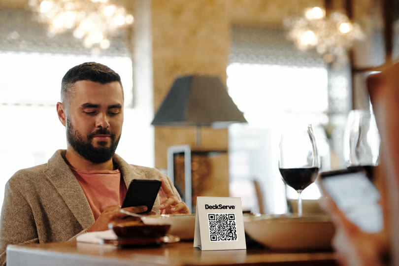A guest at a restaurant table ordering from their phone beside a DeckServe QR card